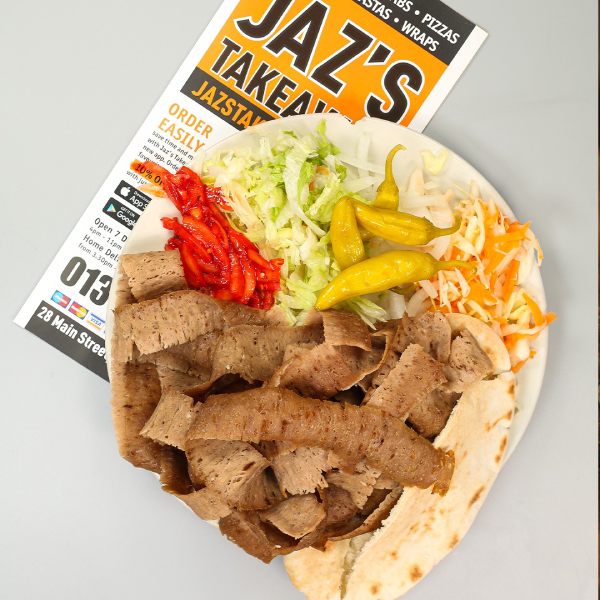 Doner kebab meat on pita bread with fresh salad, pickled peppers, and a menu flyer from Jaz's Takeaway in Crossgates